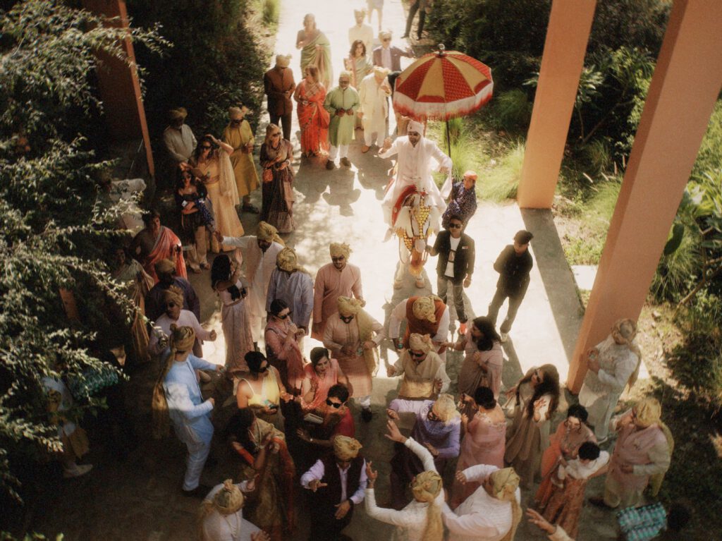 Vibrant Indian wedding procession with a groom on a decorated horse surrounded by colorful guests.